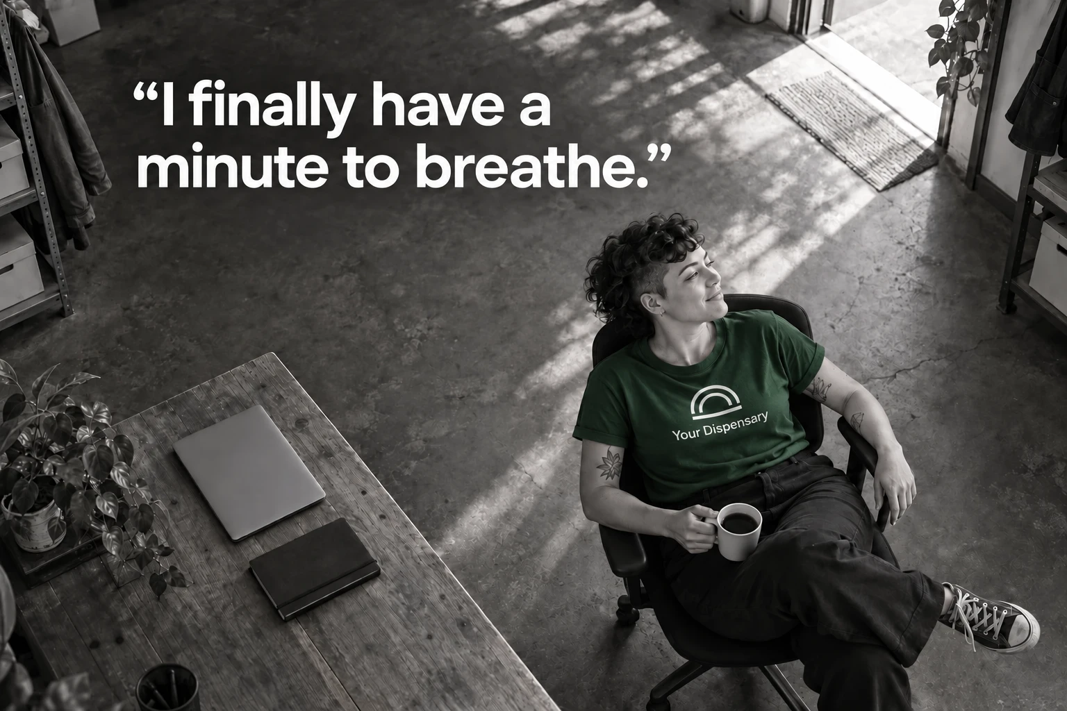 A relaxed manager in a green Your Dispensary shirt takes a break beside a closed laptop. I finally have a minute to breathe.